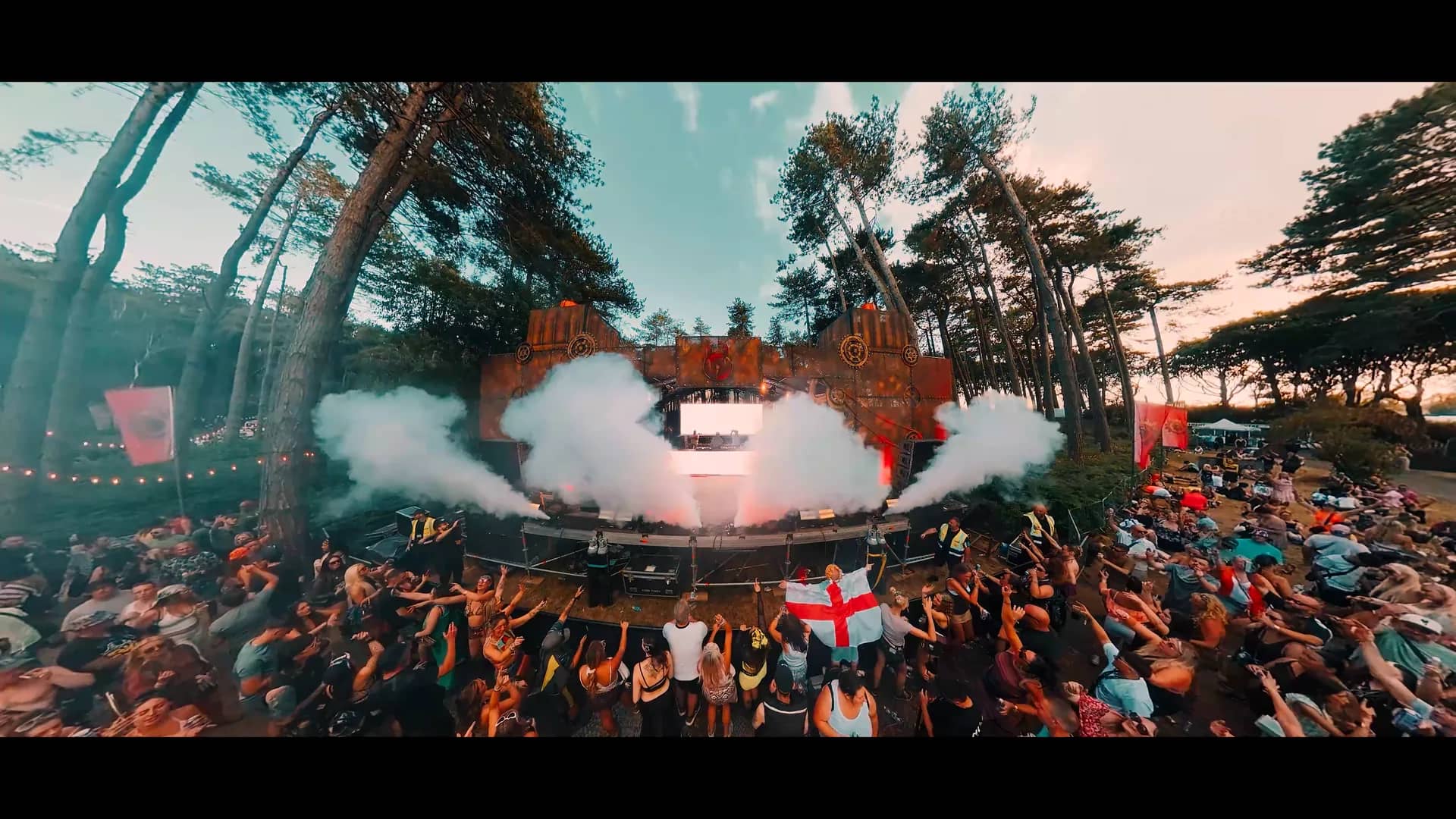 A frame from the aftermovie: CO2 plumes over the full arena with the crowd stretched back into the pines