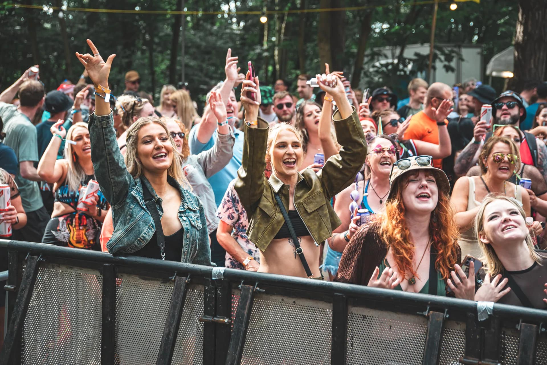 Front-row crowd at the barrier, arms up, bright daylight