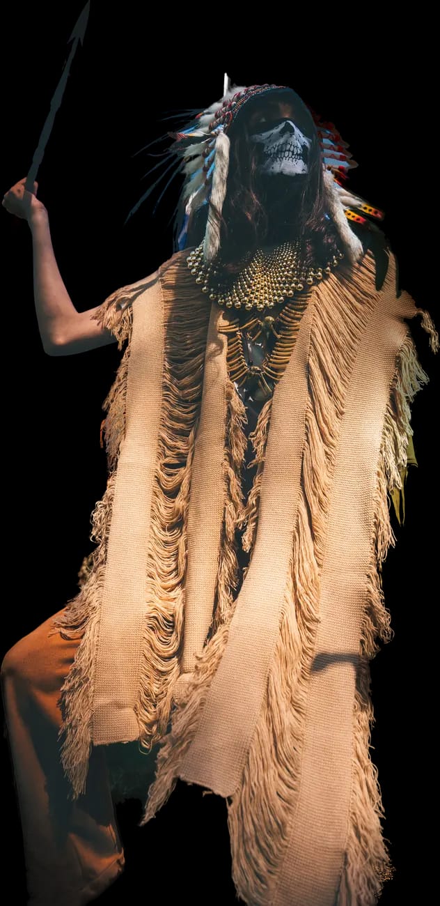 The Oracle cut out of their photograph: a feathered headdress, a skull-painted face and a raised staff.