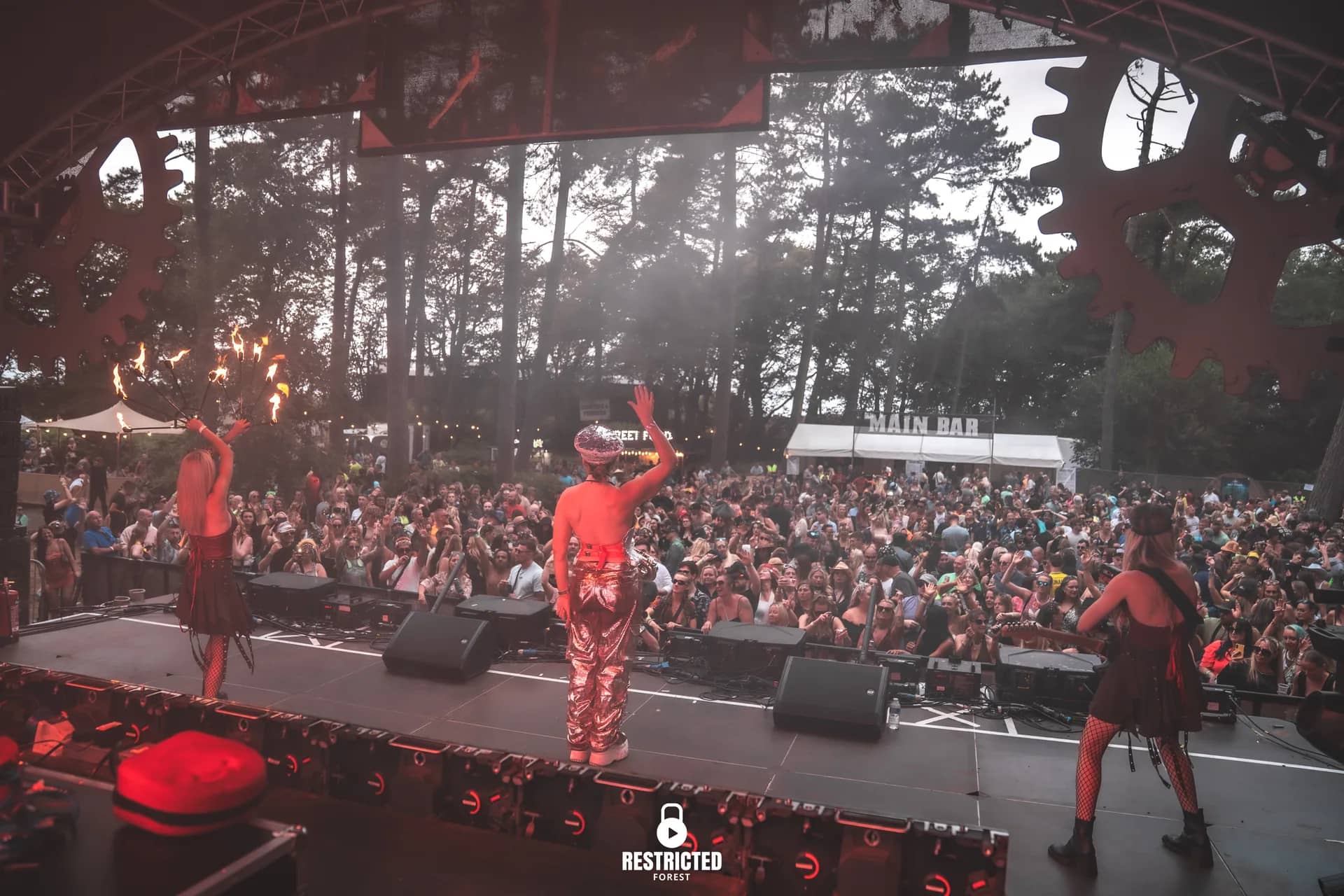 Performers on the cog-arch stage with pyro, crowd stretching back into the trees.