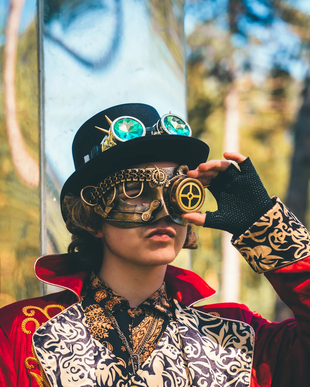 The Machinist, guardian of the Factory Realm: a red tailcoat, a brocade waistcoat and a brass-goggled top hat, photographed in the pines.