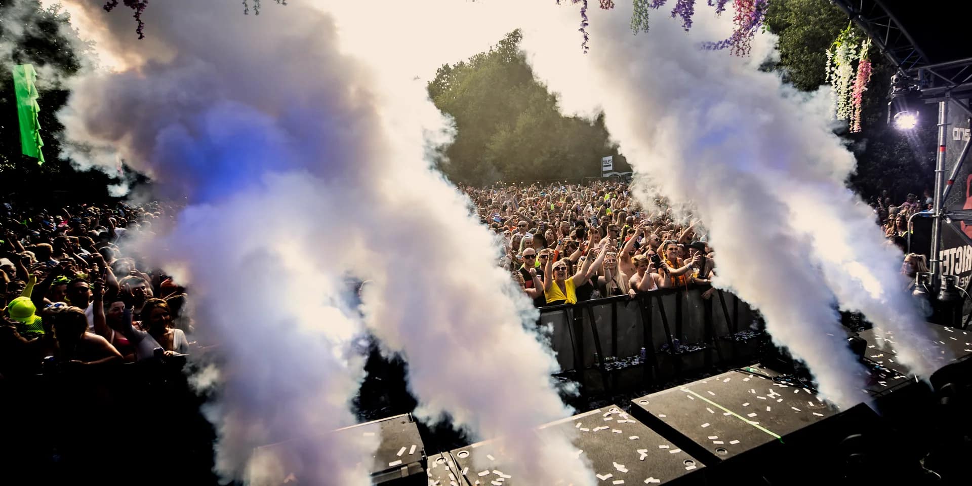 Twin CO2 jets firing over a packed daytime crowd, brick-effect stage behind