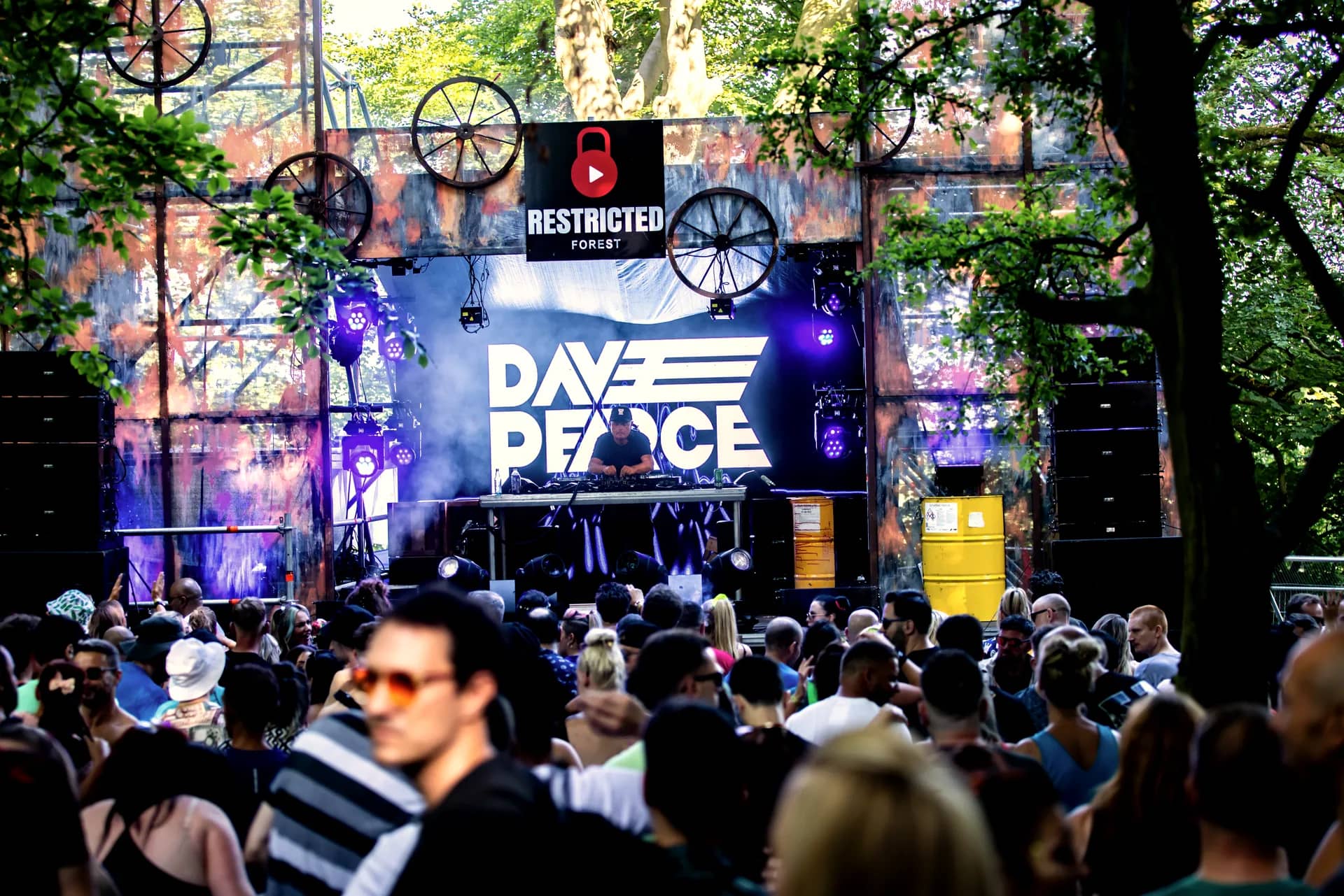 A DJ set on the cog stage in daylight, the headliner's name on the screen and the crowd close in front.