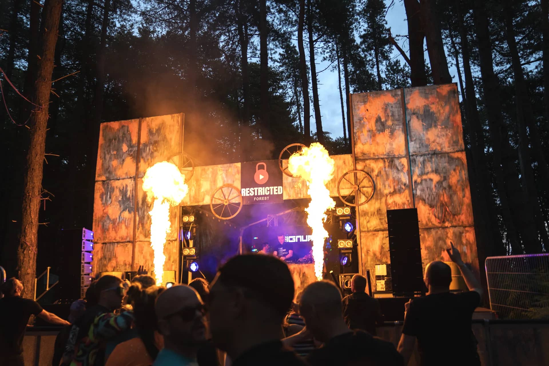Twin flame jets either side of the cog stage at dusk with the pines rising behind it.