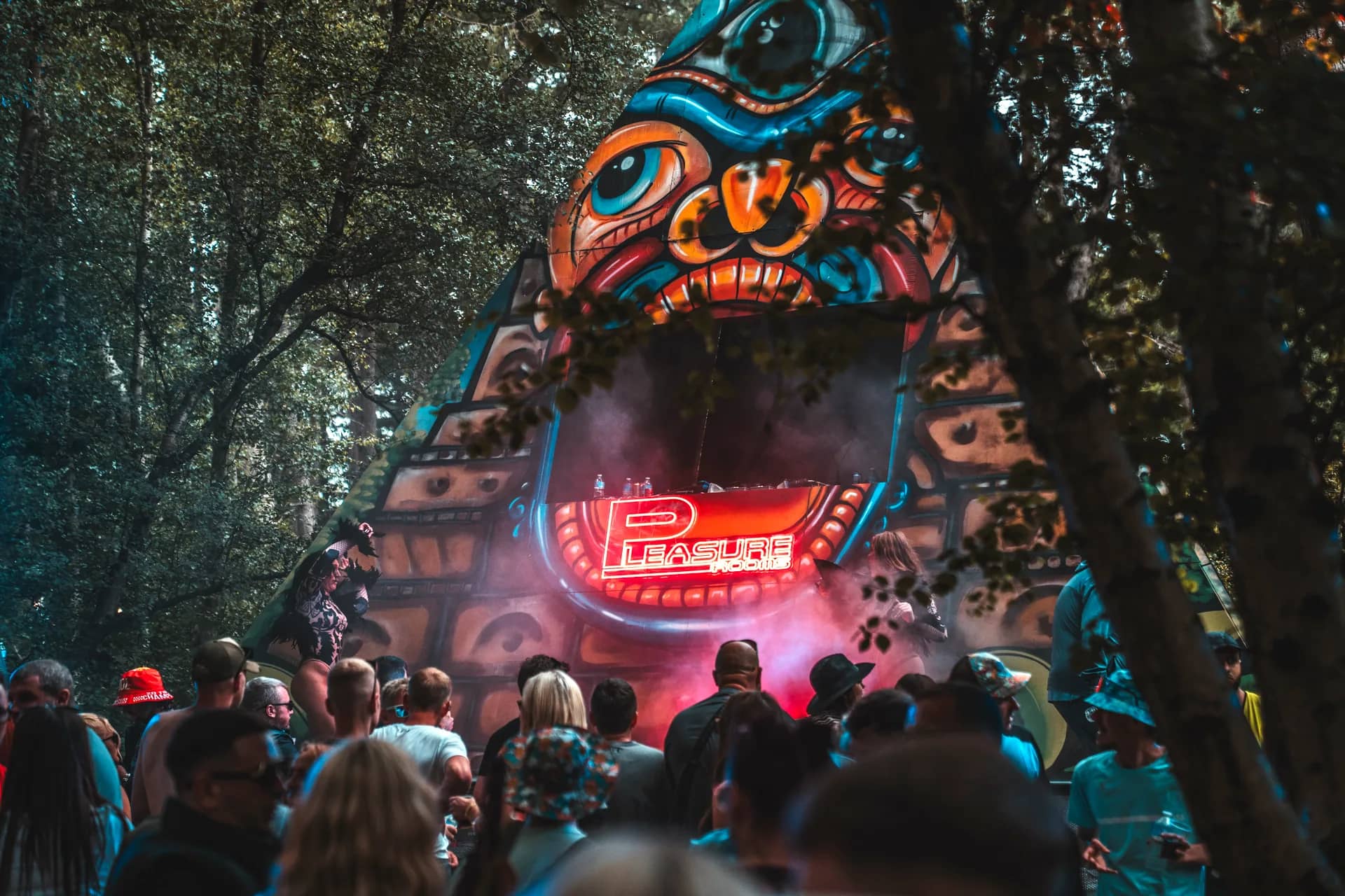 The painted pyramid stage seen through the trees, its face lit red above the crowd.