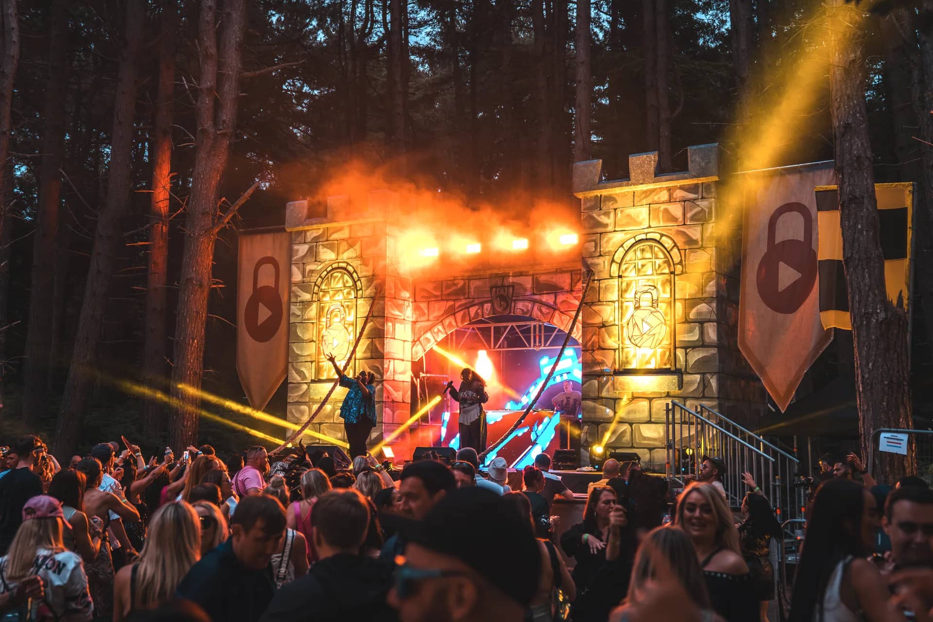 The castle stage washed gold, performers out on the deck in front of the arch and the padlock banners lit either side.