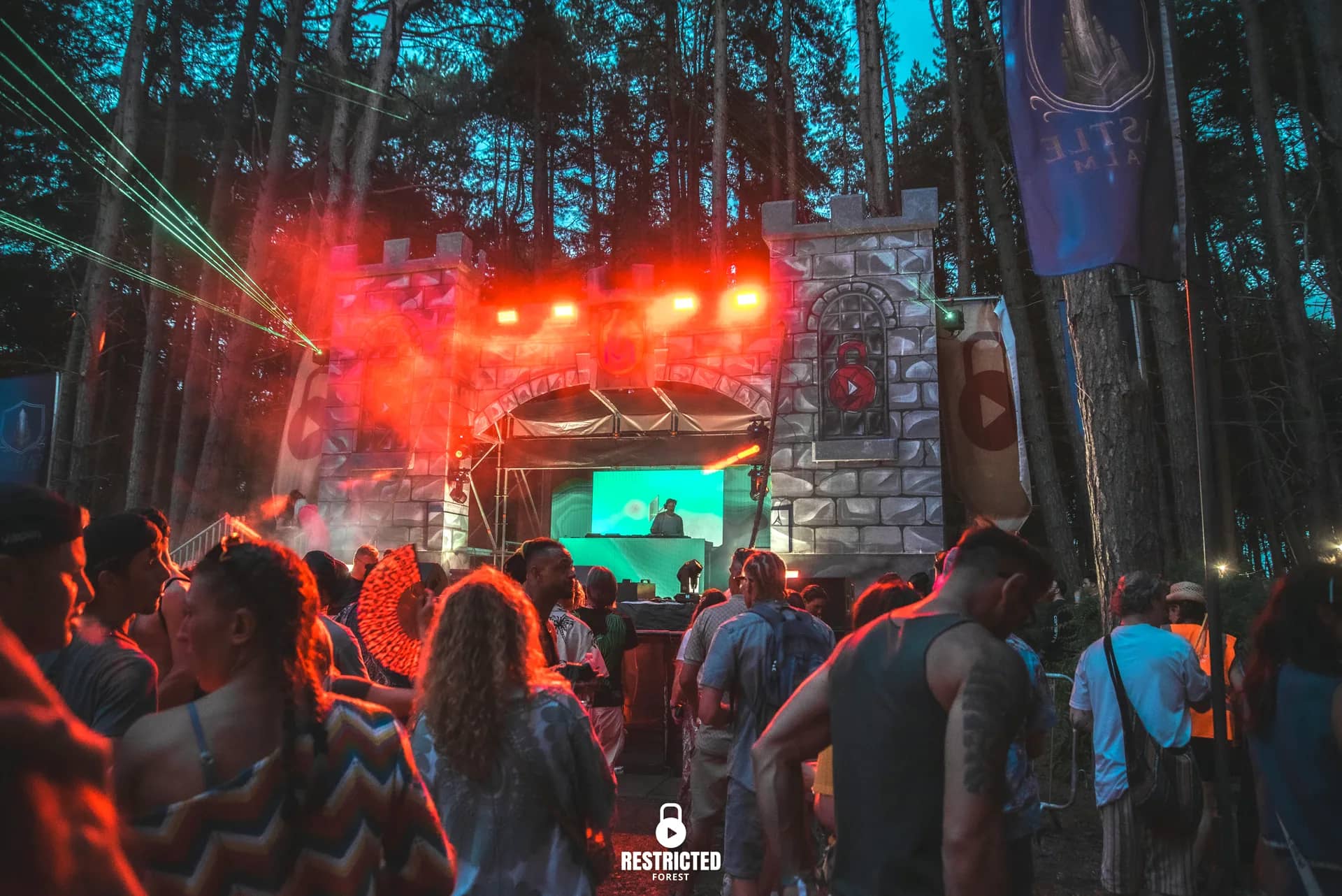 The castle stage lit red at night, the screen glowing green inside the arch and the crowd packed to the front of it.
