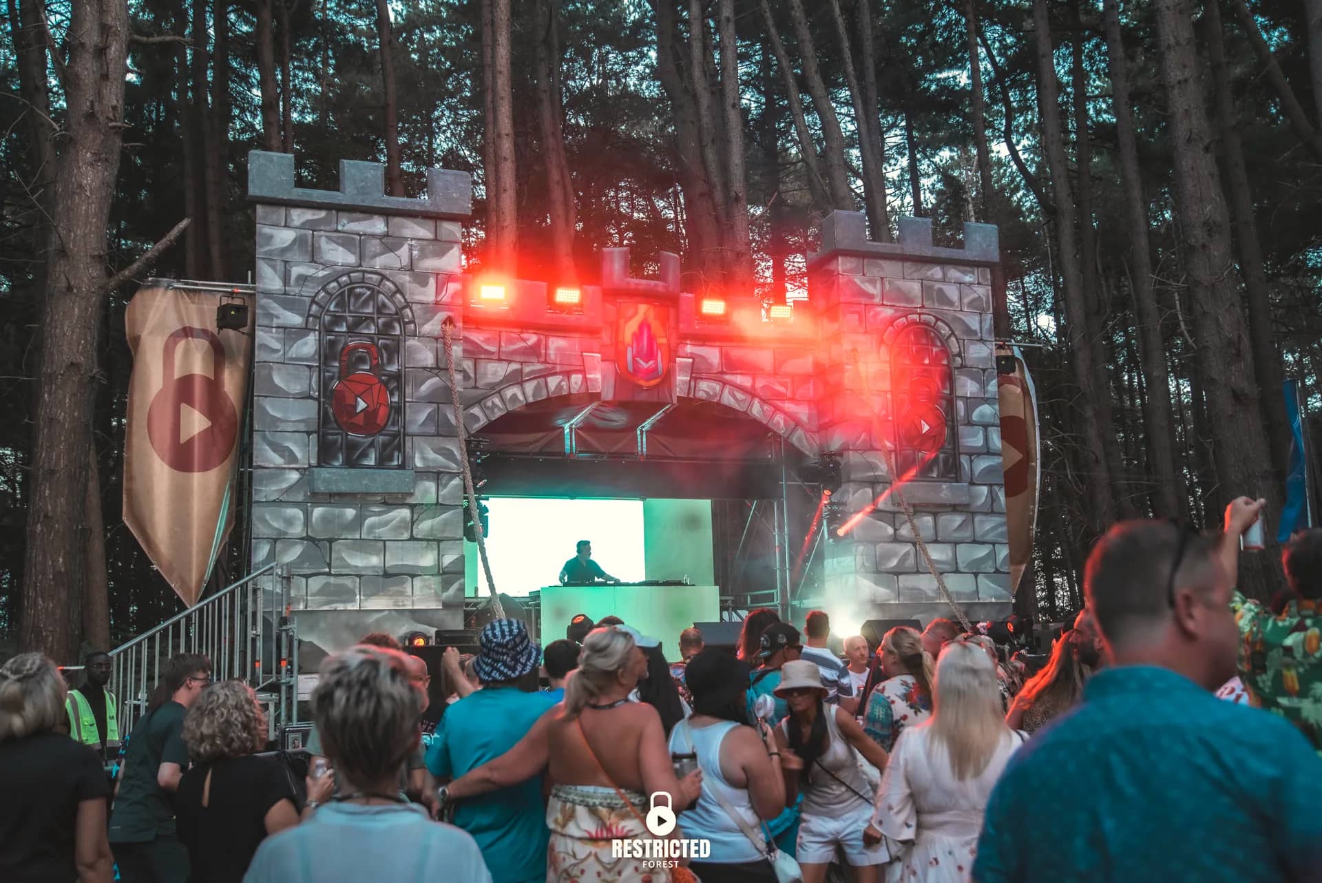 The Castle stage at dusk lit red and blue, the crowd turned toward it. Source frame RestrictedForest2026-1864.
