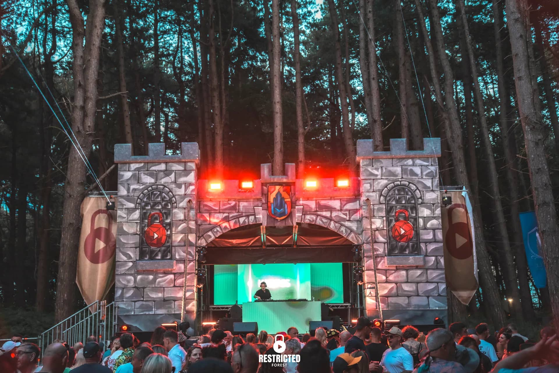 The Castle stage at dusk, the screen glowing green inside the arch under red crossbeam lights. Source frame RestrictedForest2026-1855.