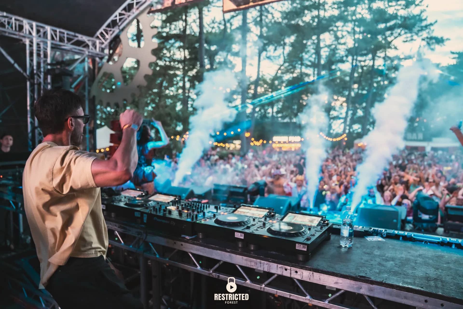 A DJ set on the factory stage at dusk, the crowd dancing through drifting smoke.