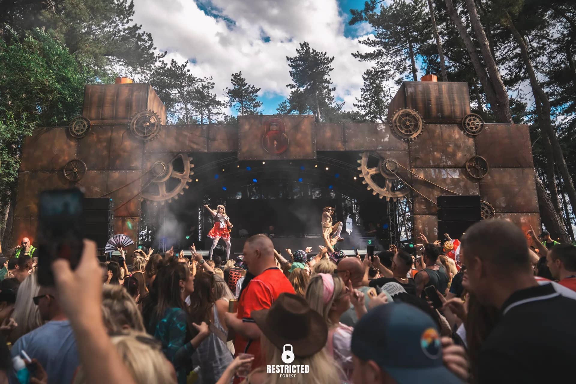 The Factory stage in daylight with white smoke drifting off the deck, phones up across the front rows. Source frame RestrictedForest2026-1345.