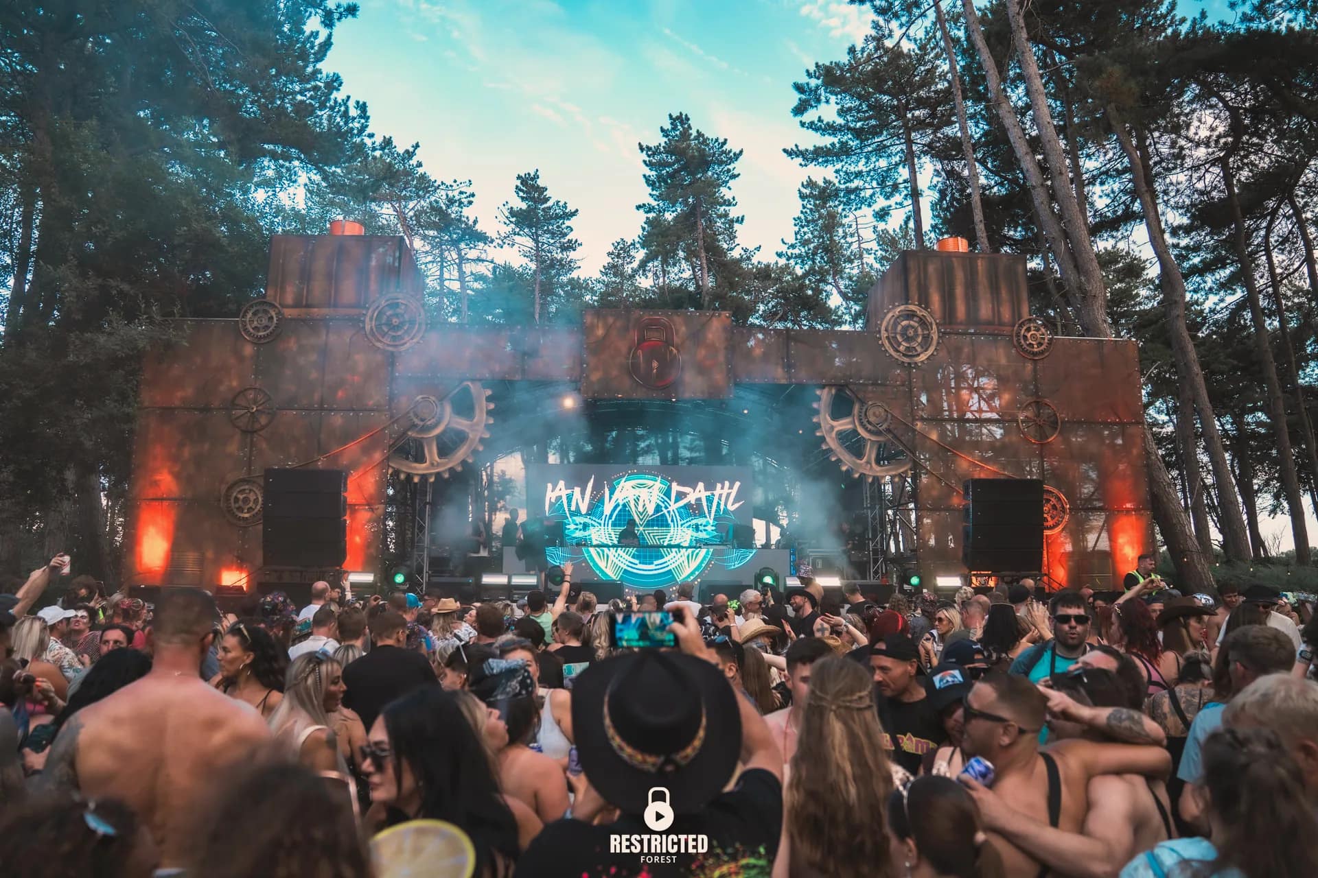 The cog and girder stage lit through heavy haze, crowd stretching back into the woods