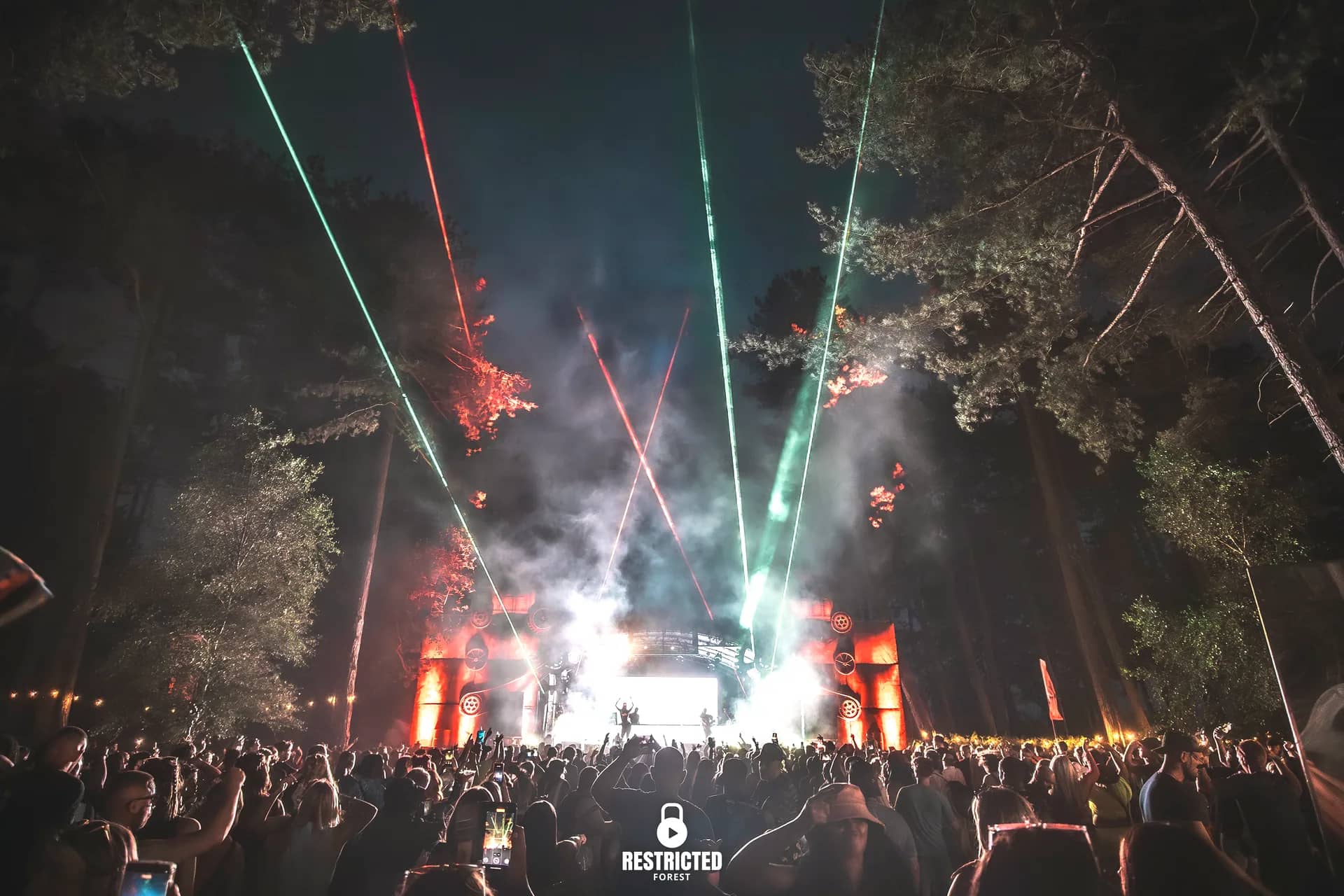 Green and red lasers fanning through smoke over the Factory stage at night, the crowd in silhouette. Source frame RestrictedForest2026-1953.