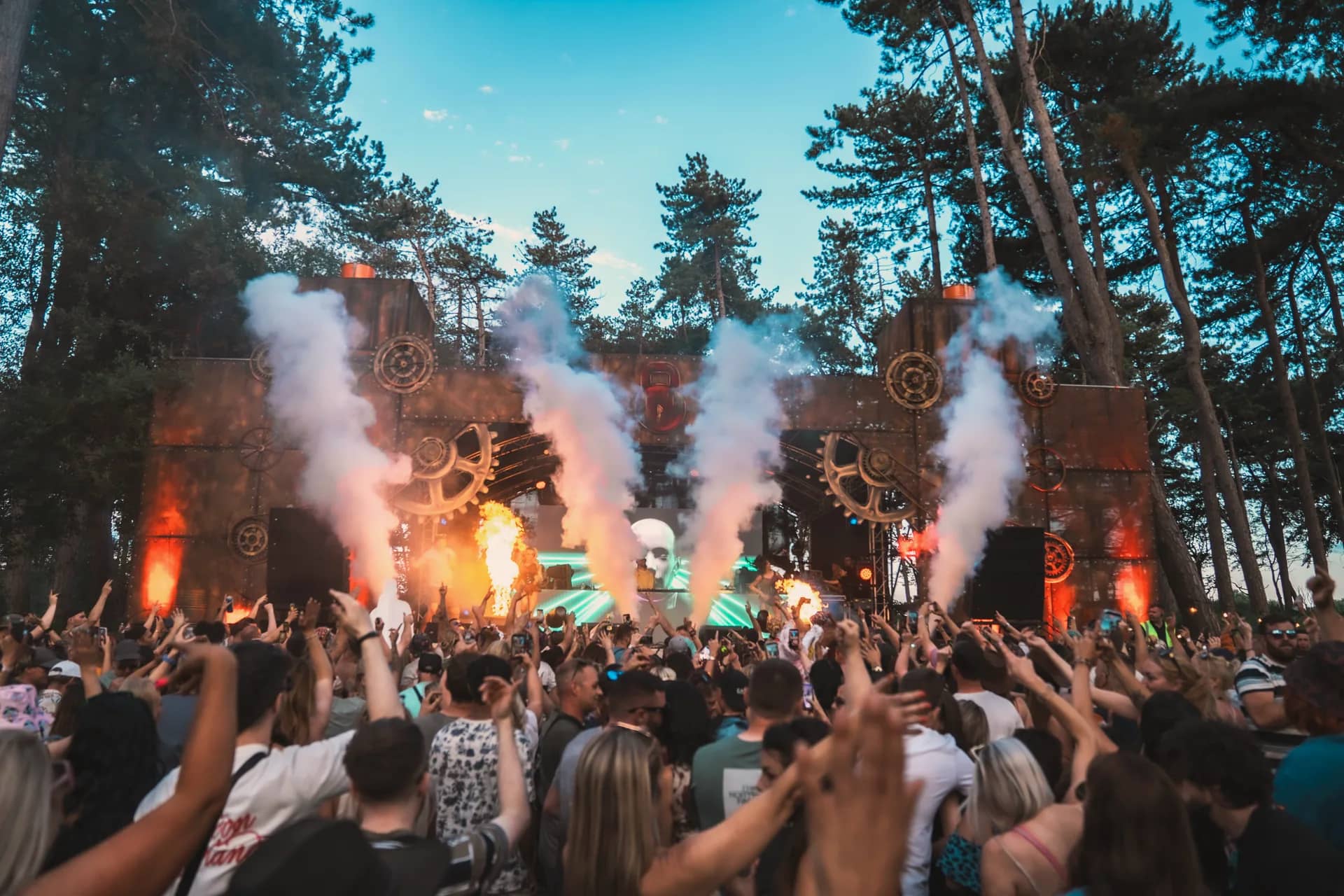 The factory gear stage lit orange at dusk with fire and smoke jets, a lit skull graphic on the screen behind the DJ.