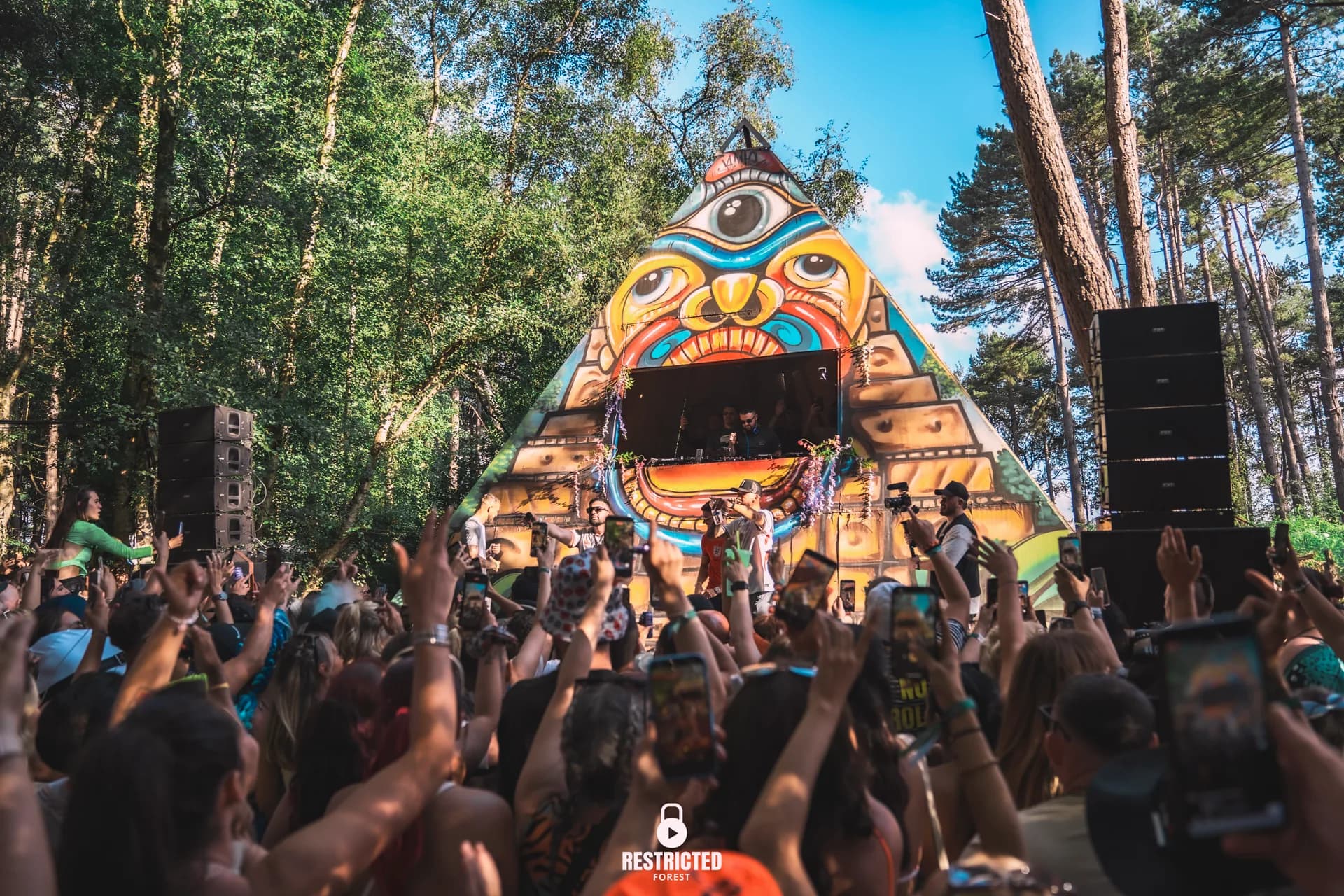 The painted pyramid stage under a clear sky, arms up across a full crowd.