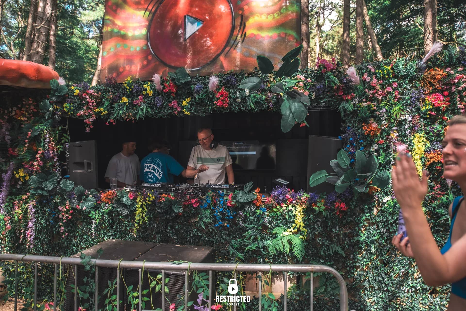 The Secret Garden booth between its toadstools in daylight, a dancer at the rail. Source frame RestrictedForest2026-1226.