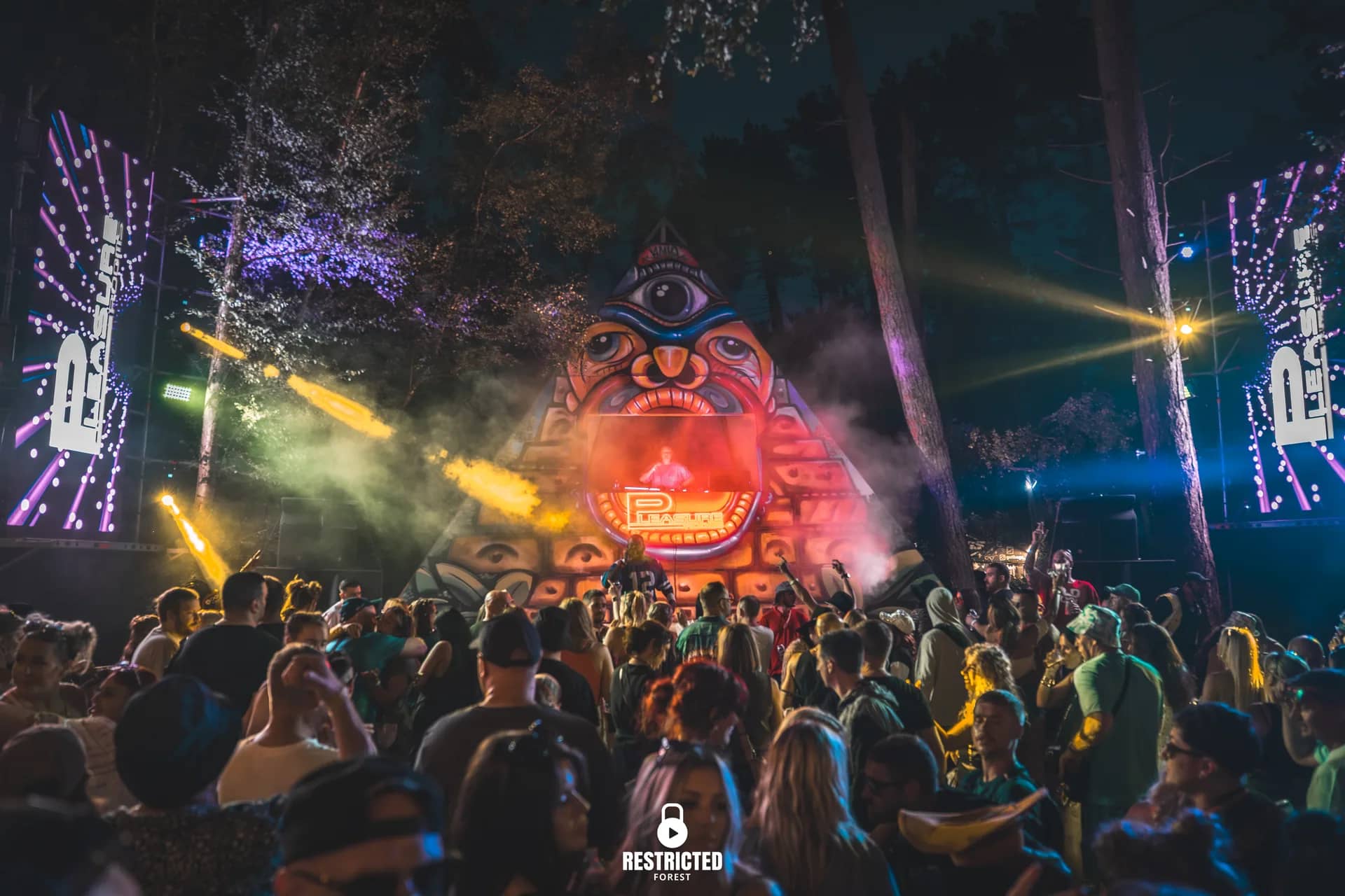 Illuminated totem face stage at night, festoon lighting strung through the trees.